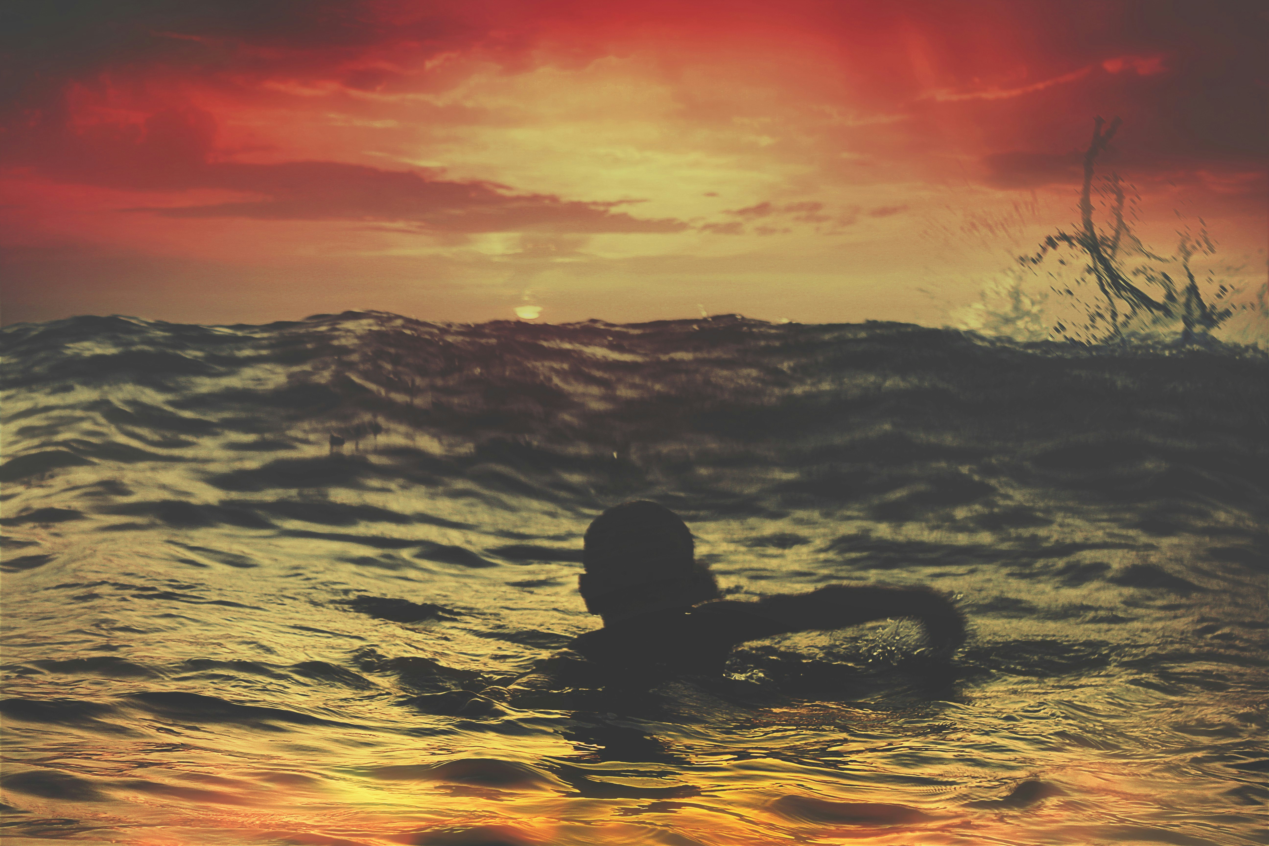 person swimming on body of water under red and orange sky